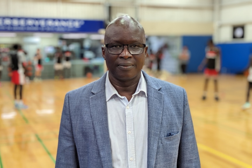 South Sudanese man wearing a blue suit standing on a basketball court.