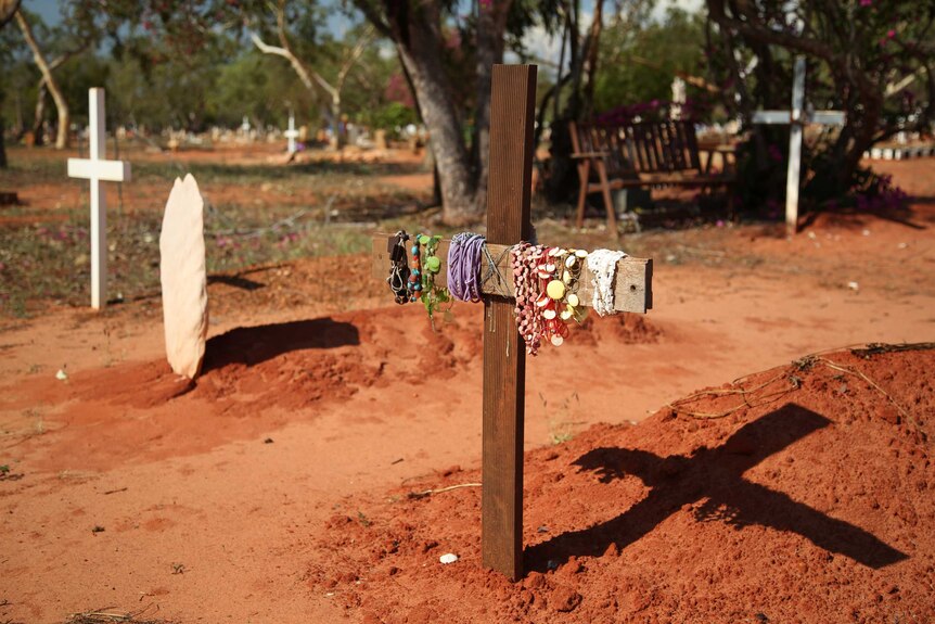 A cross with bracelets hanging off it in the dirt marking a grave at Broome cemetery.