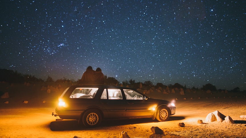 a couple on top of a car looking at the stars