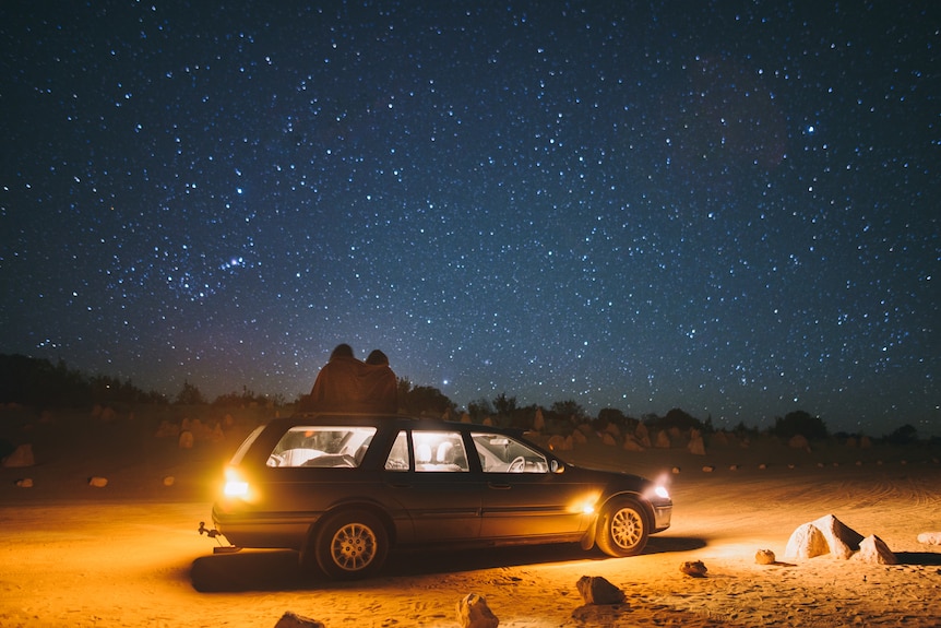 a couple on top of a car looking at the stars