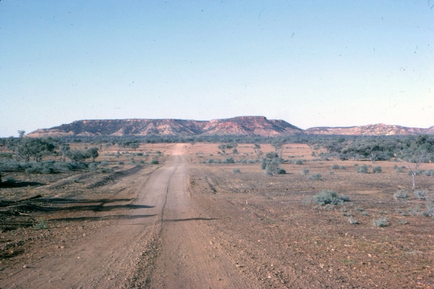 Un chemin de terre en arrière-plan avec des collines rocheuses et un ciel bleu en arrière-plan