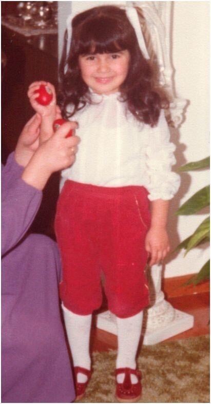 A young girl with a white ribbon in her hair holds a red Easter egg