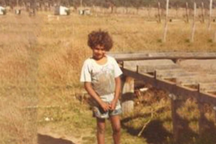 Young boy who is Indigenous standing in a dry grass paddock