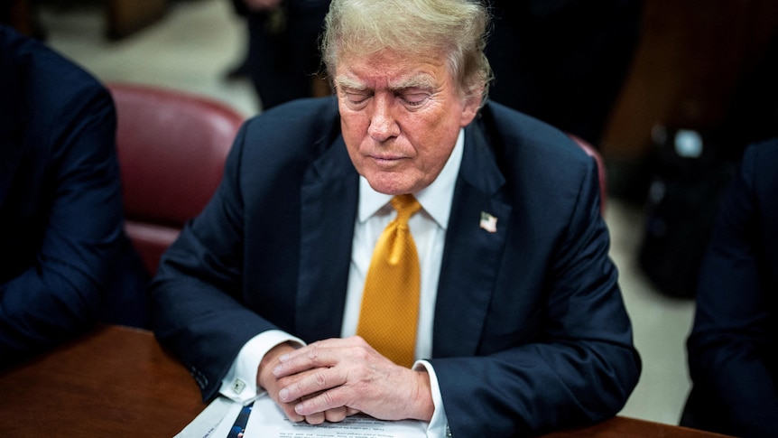 Trump looks down frowning while wearing a suit in court