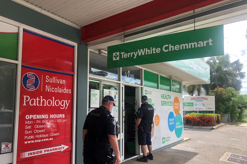 Two police officers in uniform standing outside a green pharmacy building in Townsville.
