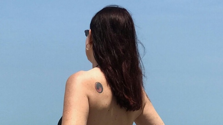 Noriel who is an escort in Cairns wearing a swim suit and looking out to sea with her back to camera.