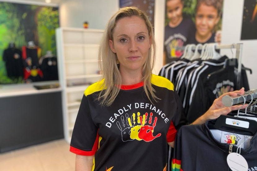Angela wearing a black shirt, printed with black, yellow and red handprints and the words "Deadly Defiance".