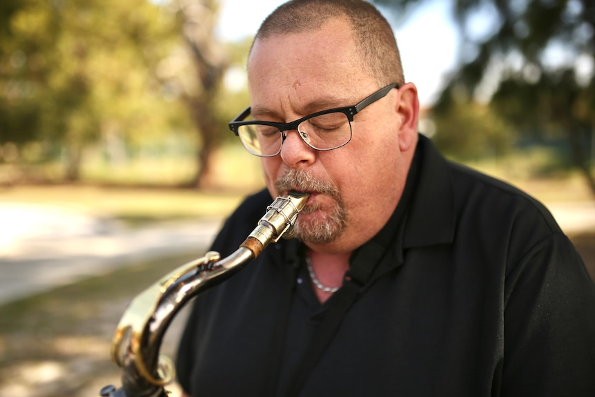 Andrew Fairbairn playing sax in a park.