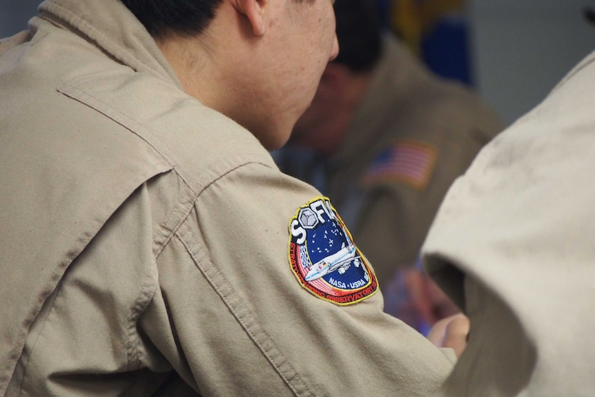 Looking over the shoulder of a man who is wearing a NASA jumpsuit with a SOFIA patch on it.
