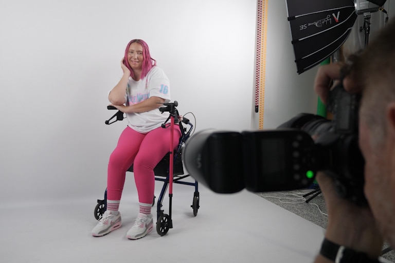 woman in pink tights on a mobility frame sitting as a man takes her photo