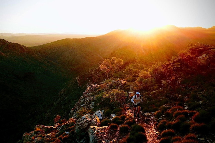 Sun casting red light on mountains with a runner in the distance running towards camera.