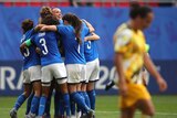 Italian players celebrate in a huddle as an Australian player walks with her head down in the foreground.