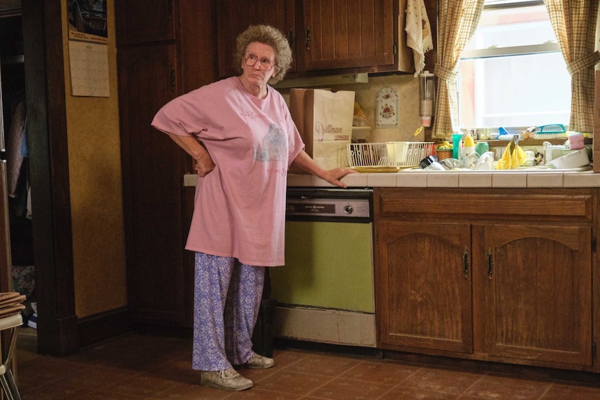 A woman with grey hair is standing at a kitchen bench