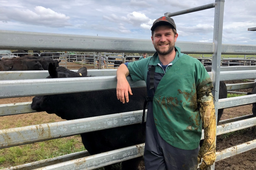 Young man in vet uniform holds an ultrasound probe and poses against cattle yards