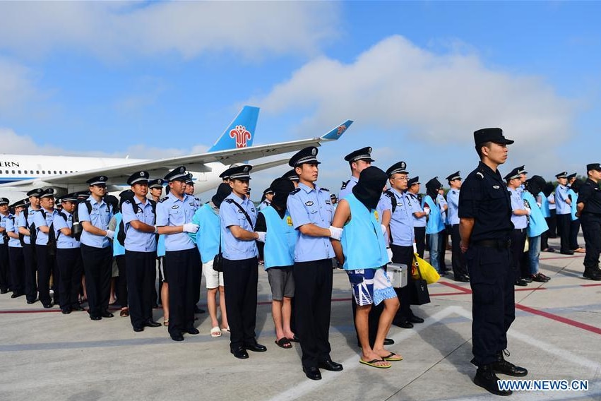 Hooded, handcuffed Chinese fraud suspects arrive at a Chinese airport under heavy police guard. They are lined up on the tarmac