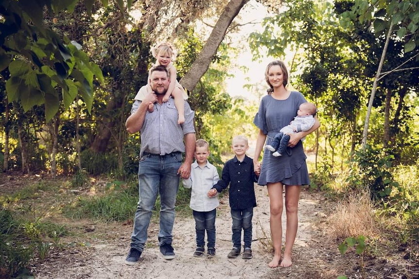 A man and woman with four children standing in a line on a dirt path in a forest