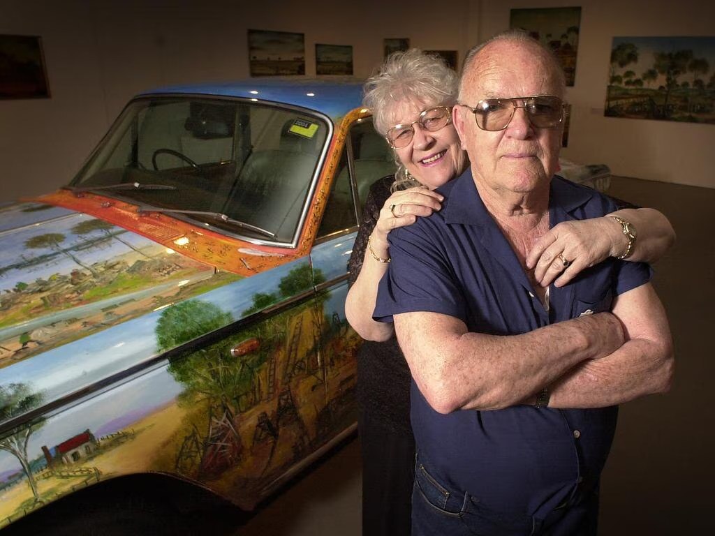 A woman and a man in front of a vintage car in a garage.