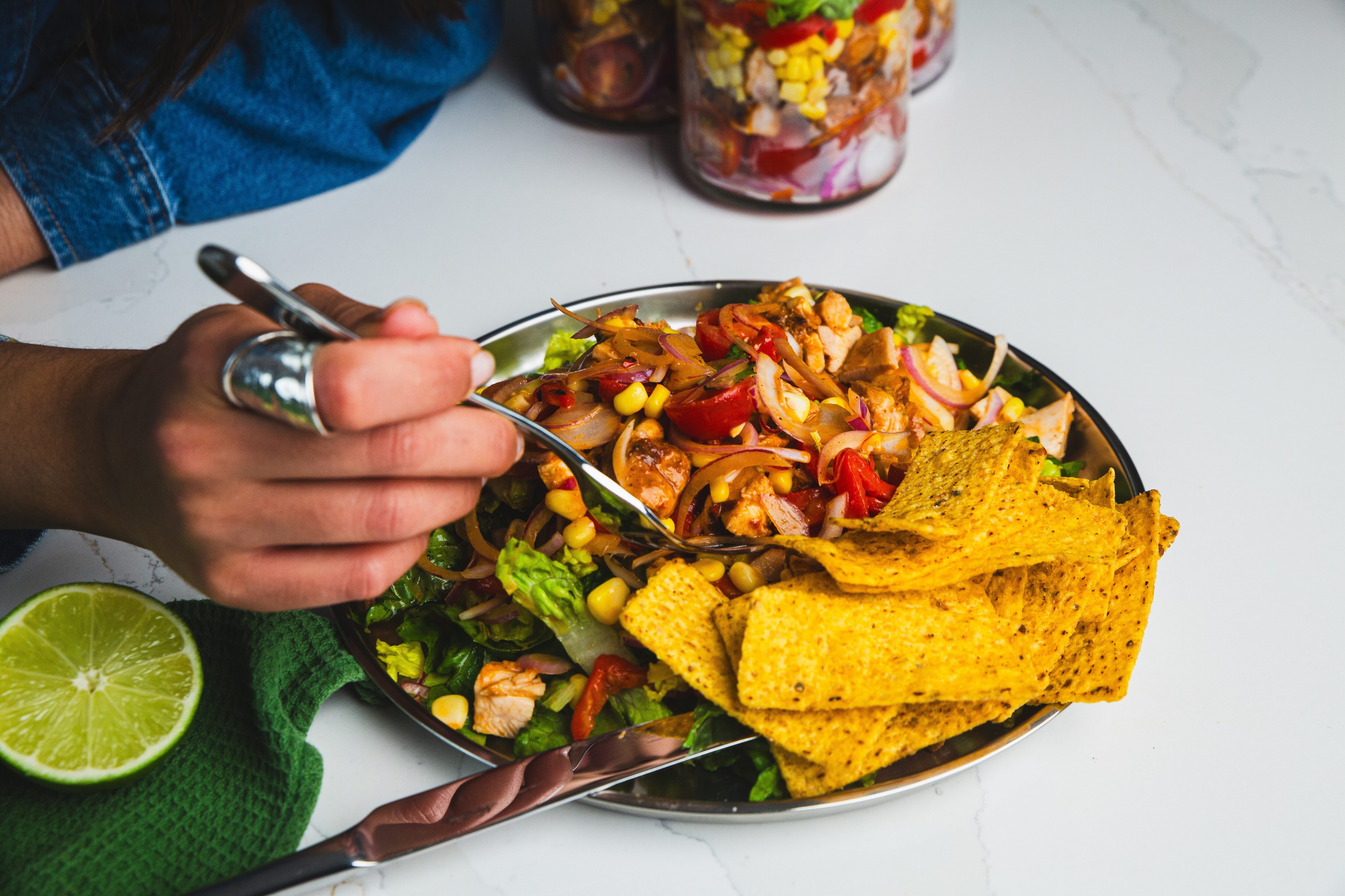 Una mujer come una ensalada de pollo al chipotle mexicano con un tenedor, servida con chips de maíz.