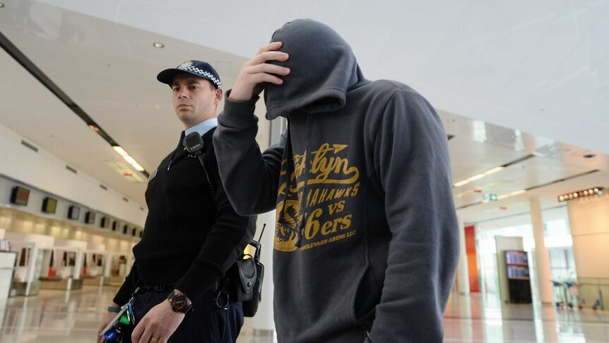 Christopher Hill is escorted by police to a plane at Canberra Airport.