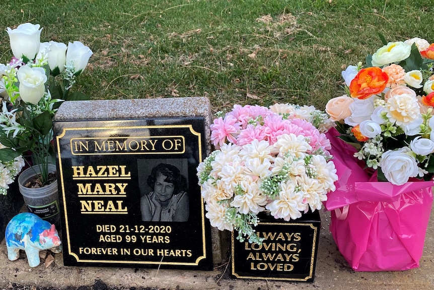 A black headstone which reads "Hazel Mary Neal" in gold lettering, surrounded by three bunches of flowers.