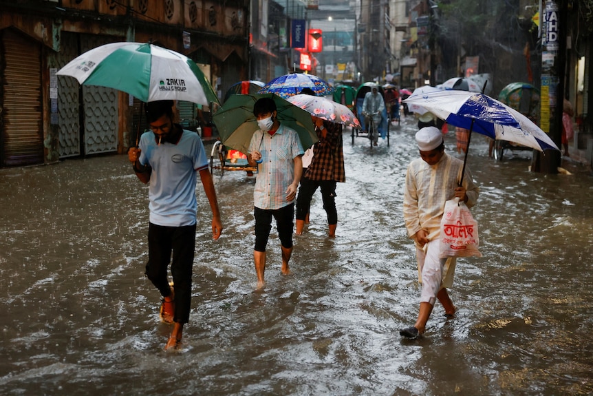 People with umbrellas walk through ankle deep water on a flooded street.