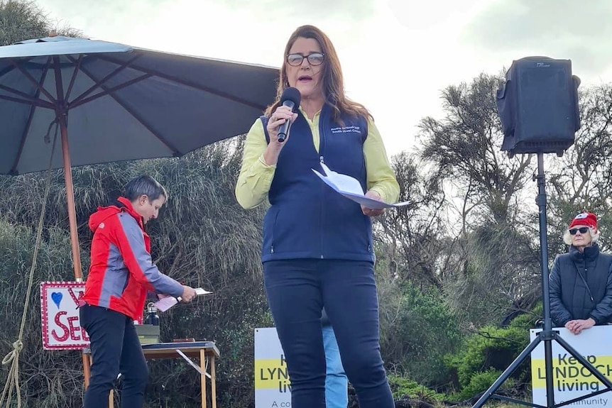 Woman with brown hair speaks to crowd with microphone.