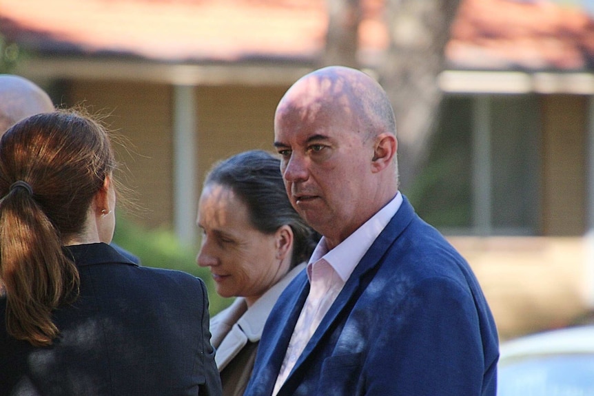 Bald man in blue suit talks with two women