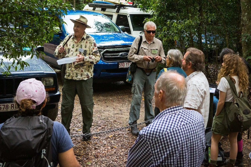 One man speaks to a group of men and women who stand in the rainforest of the Cooloola Coast.