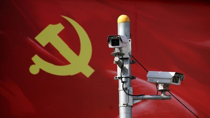 Security cameras on a pole, in front of the red Communist Party flag.
