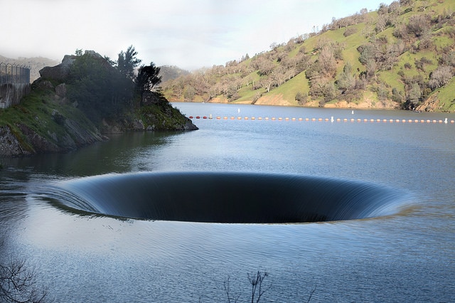 A view across a lake with a giant drain emptying water from the middle of it