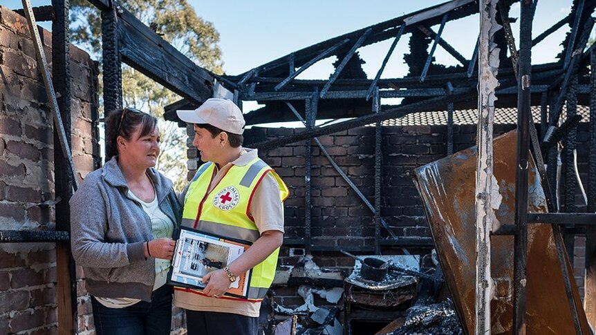 Red Cross worker and woman stand in burnt down home
