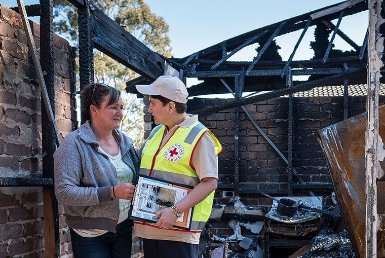 Red Cross worker and woman stand in burnt down home