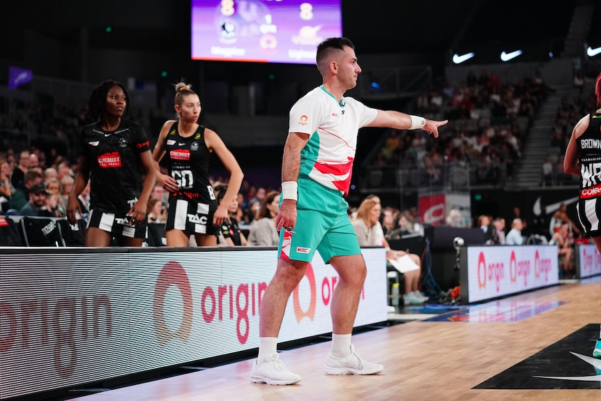 A Super Netball umpire points to the spot where the penalty should be taken.