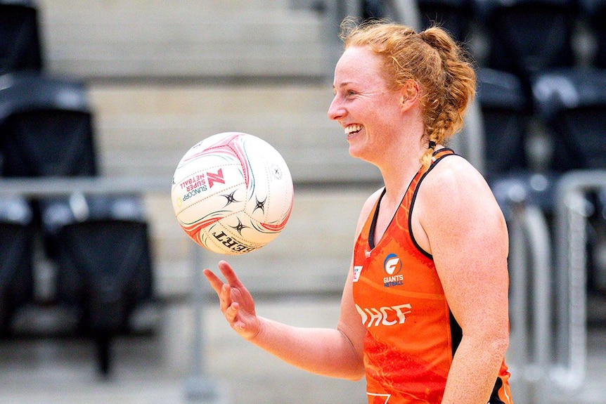 Sam Winders plays with a ball and smiles on a netball court 