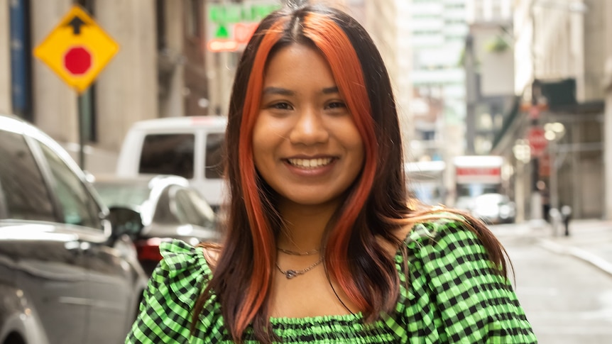 A portait of a young woman in a city street. She's wearing a bright green checked shirt. 