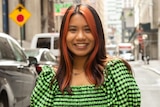 A portait of a young woman in a city street. She's wearing a bright green checked shirt. 