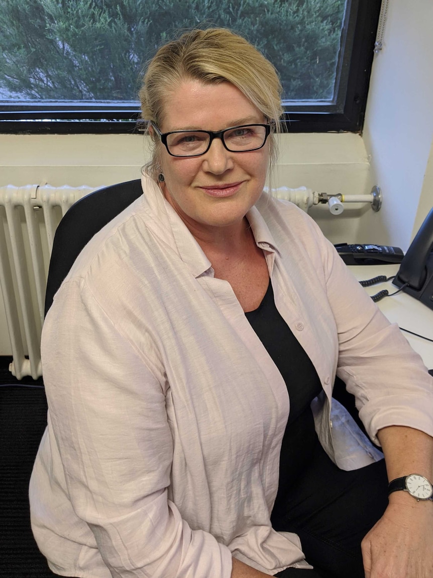 A woman with black glasses sits at a computer