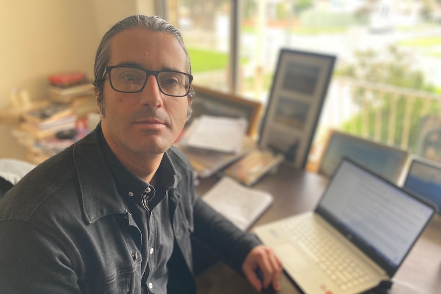 A man sitting at a desk with a laptop computer on it in front of a window