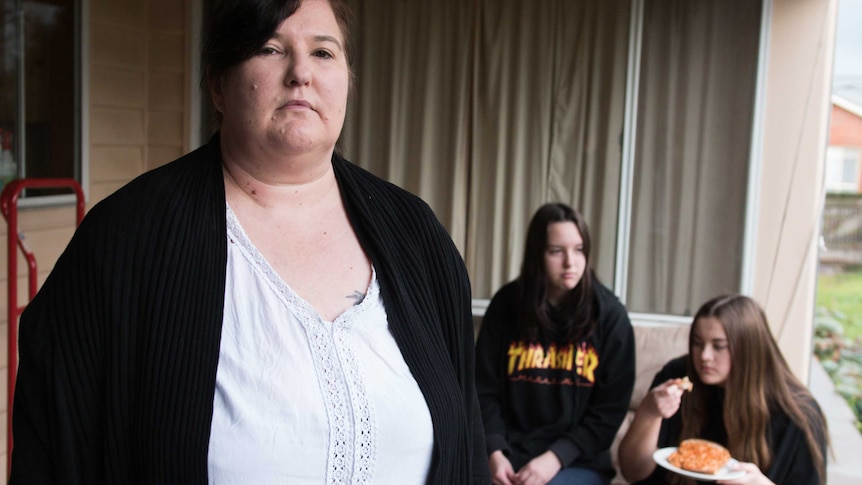Mandy Weber stands with her daughters Olivia and Mariah sitting eating baked beans in the background.