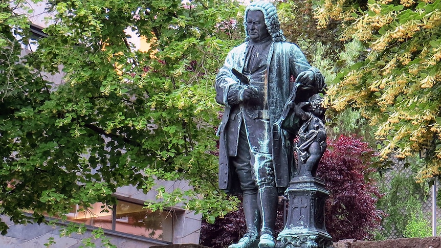 A bronze statue of the composer Johann Sebastian Bach with trees in the background.
