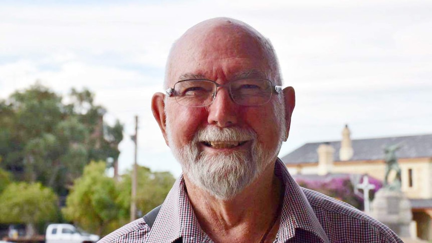 Peter wears glasses and has a moustache he smiles to the camera on a street in Broken Hill