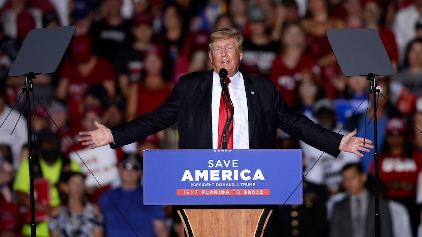 Donald Trump stands on stage behind a lectern that says "Save America" 