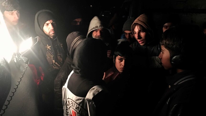 Syrians cluster around a woman wearing a Red Cross vest.