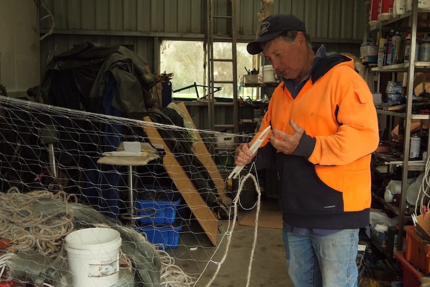 A man in an orange top fixes a fishing net in a shed