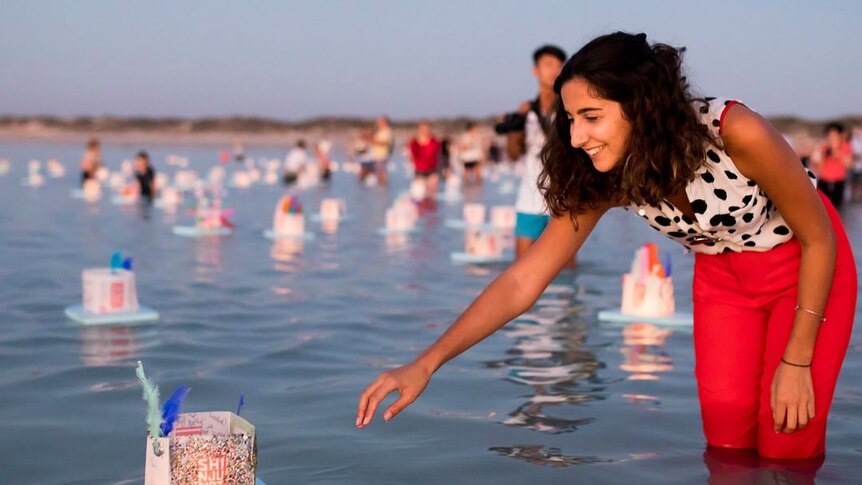 A woman floats a lantern in the ocean