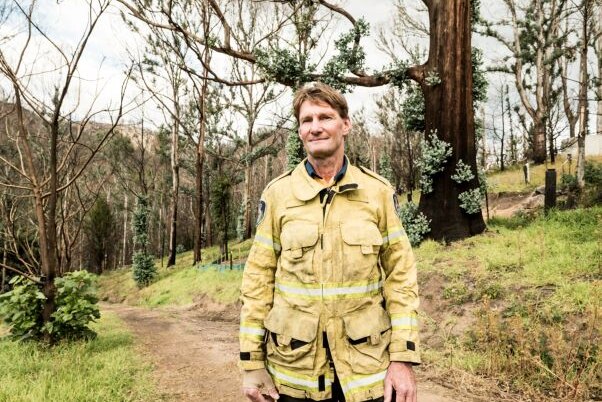 Man in Rural Fire Service uniform with bandaged hand standing on burnt property