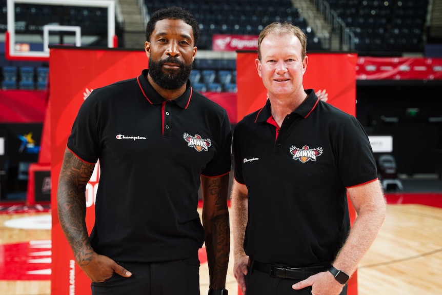 Justin Tatum and Mat Campbell stand side by side wearing black and red polo shirts on a basketball court.