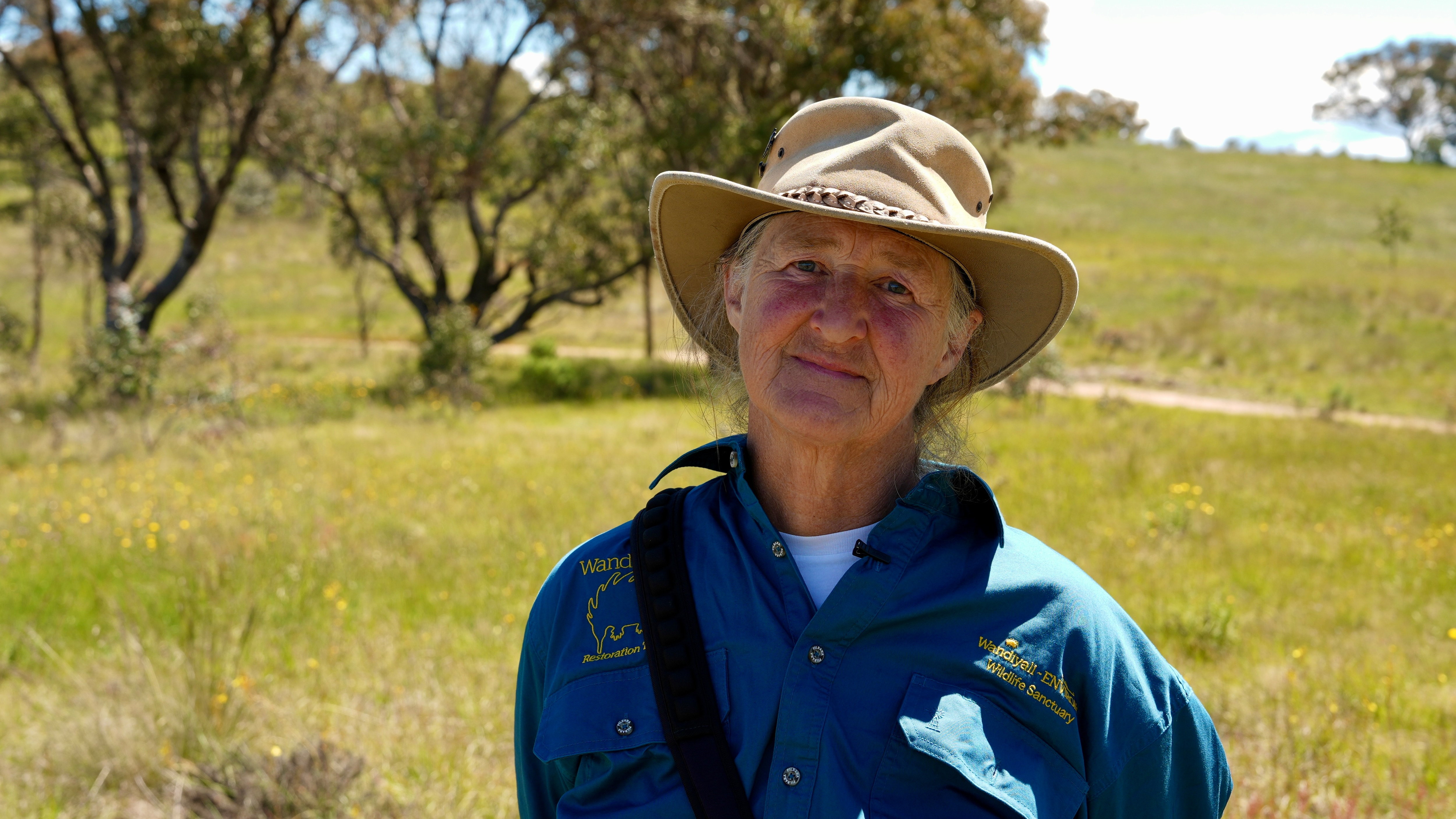 A woman wearing an akubra standing on a bush property looking frustrated.