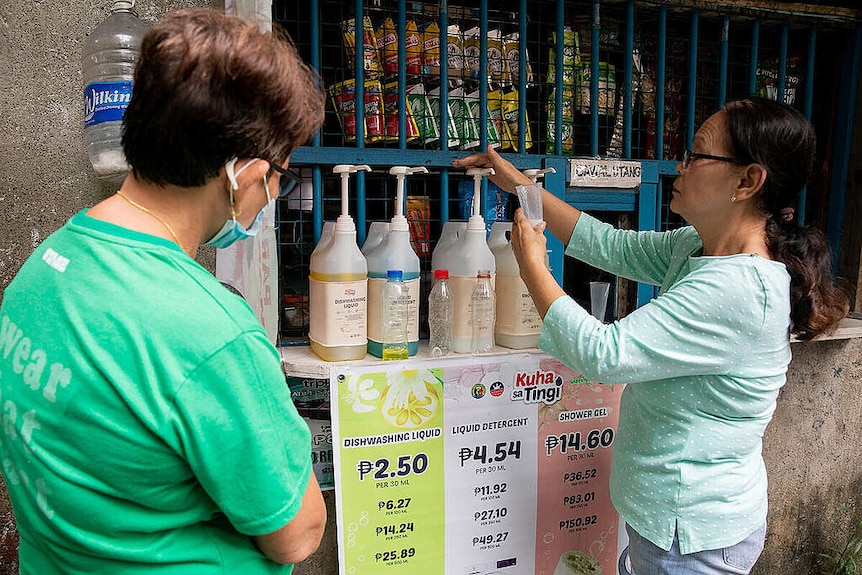 Two women in front of the stall, one of whom is filling a container from a refillable pump bottle.