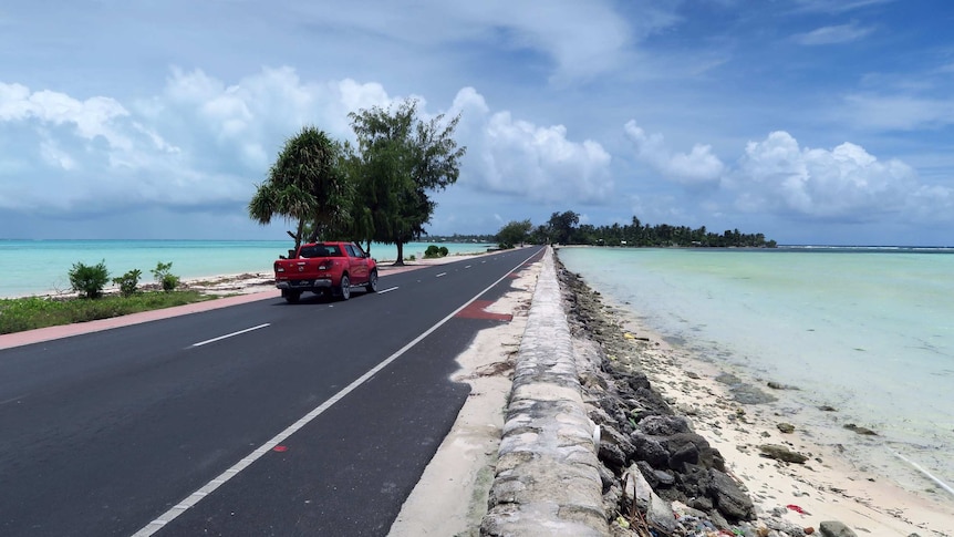 A new-looking bitumen road connecting one island to another, with a build-up of sand and rocks on either side.